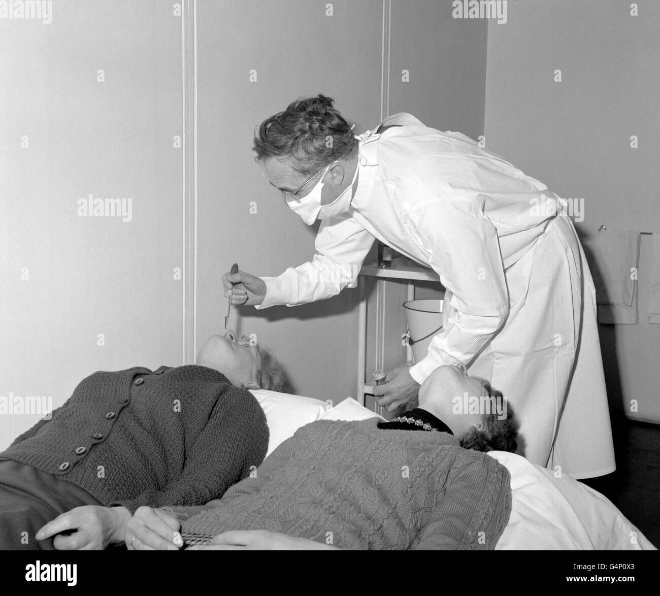 Dr. D.A.J. Tyrrell, Leiter der Abteilung, wirft ein häufiges Erkältungsvirus in das Nasenloch der freiwilligen Patientin Frau Swallow, während Mitpatientin Miss E.A. Hollister wartet an der Reihe am Harvard Hospital. Stockfoto