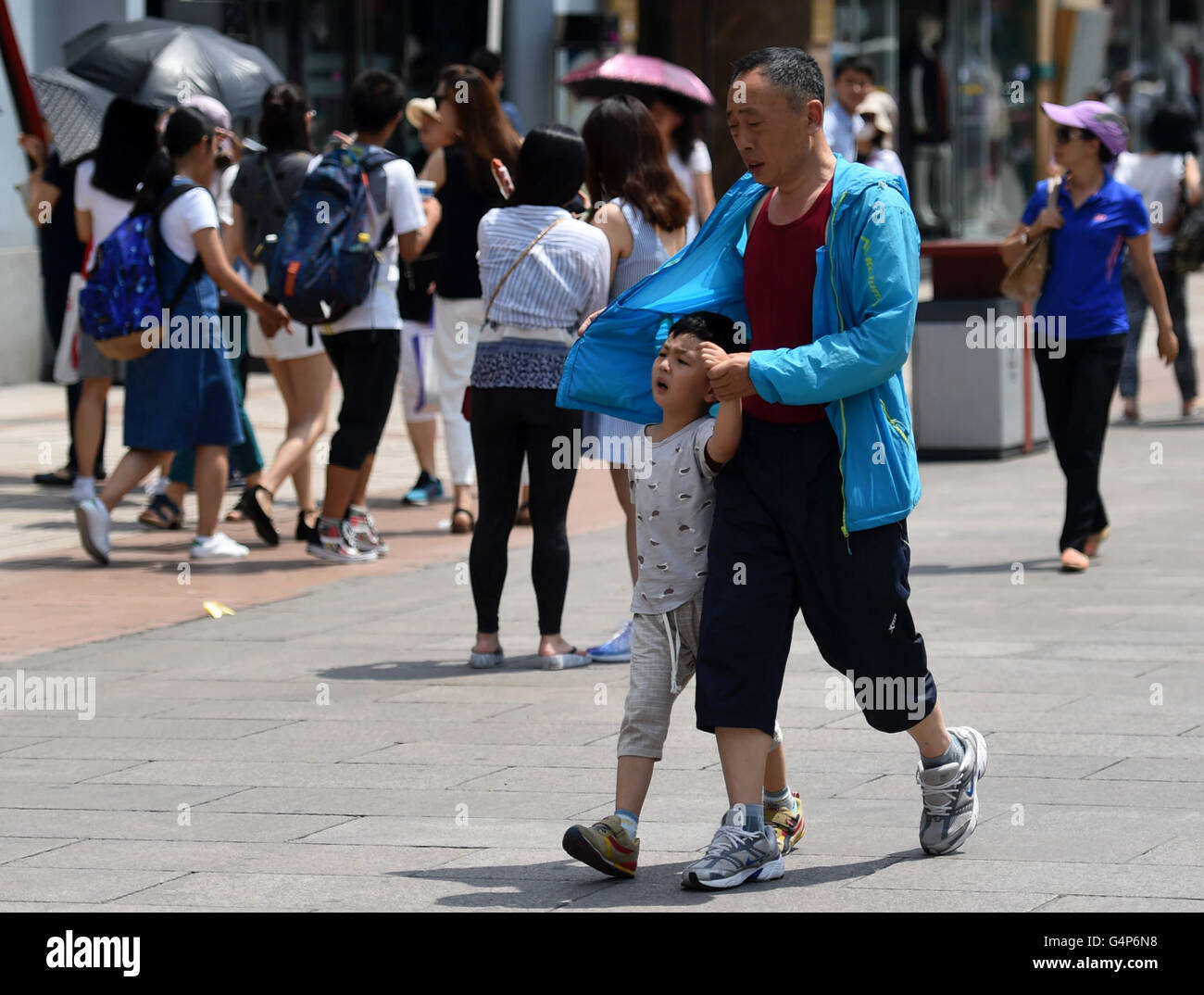 (160619)--Peking, 19. Juni 2016 (Xinhua)--ein Mann nutzt seinen Mantel um sein Kind auf einer Straße in Peking, Hauptstadt von China, 19. Juni 2016 schattieren.  Die höchste Temperatur von Peking erreicht 35 Grad am Sonntag. (Xinhua/Zhang Chenlin) (Wjq) Stockfoto