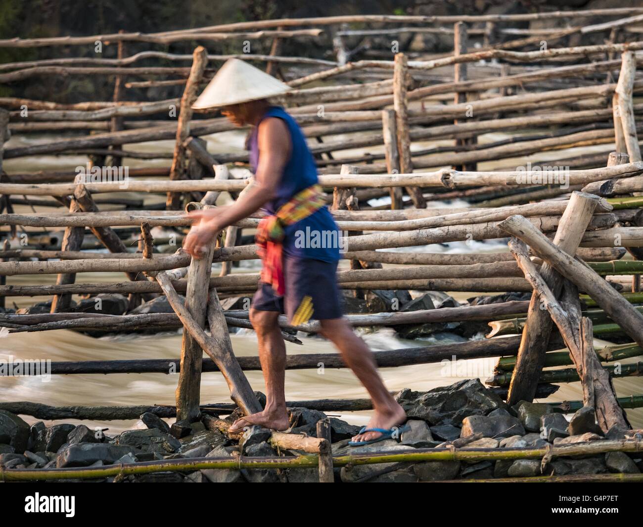 19. Juni 2016 - Don Khone, Champasak, Laos - Spaziergänge entlang der Seite eines seiner Reusen bei Khon Pa Soi Wasserfällen, auf der Ostseite des Don Khon ein Fischer. Es ist die kleinere der zwei Wasserfälle in Don Khon. Fischer haben ein ausgeklügeltes System von Hängebrücken über die Fälle konstruiert, die sie benutzen, um die Fischfallen, die sie gesetzt. Fischer in der Gegend sind mit geringeren Erträgen und kleinere Fische, streitenden ihre Art zu Leben bedroht. Der Mekong ist eines der artenreichsten und produktivsten Flüsse auf der Erde. Es ist ein globaler Hotspot für Süßwasserfische: mehr als 1.000 Arten registriert Stockfoto