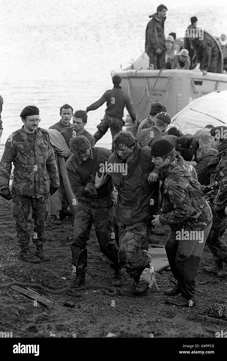 DER FALKLAND-KRIEG: Hilfe für einen verletzten Gefährten als Überlebende in Bluff Cove, East Falkland, an Land kommen, nachdem zwei britische Landungsschiffe, Sir Galahad und Sir Tristram, während des Falkland-Konflikts angegriffen wurden. Stockfoto