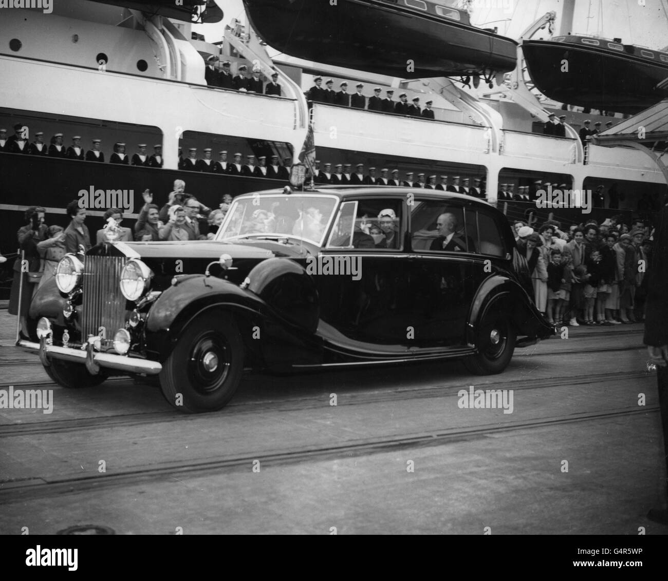 Königin Elizabeth II. Winkt den Zuschauern zu, als sie bei ihrer Rückkehr mit dem Herzog von Edinburgh von einem dreitägigen Besuch auf den Kanalinseln von der Royal Yacht Britannia in Portsmouth abfährt. Der Herzog war mit dem Lastkahn zur HMS Vernon abgereist Stockfoto