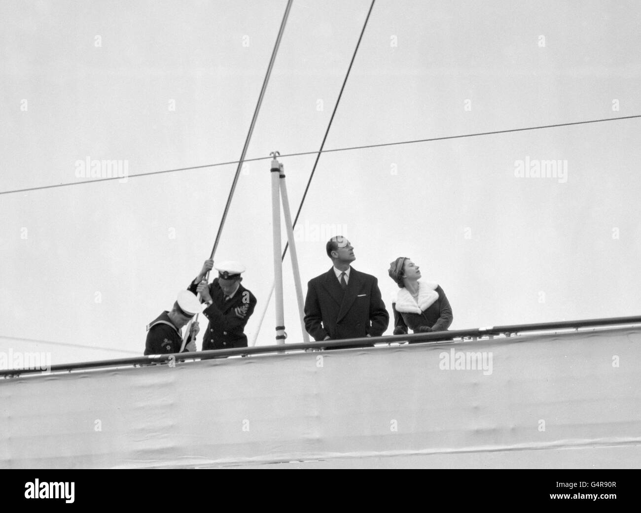 Königin Elizabeth II und der Herzog von Edinburgh sehen auf, wie der Royal Standard am Hauptmast der Royal Yacht Britannia gebrochen wird, bevor sie zu ihrem dreitägigen Staatsbesuch nach Holland aufbrechen. Stockfoto