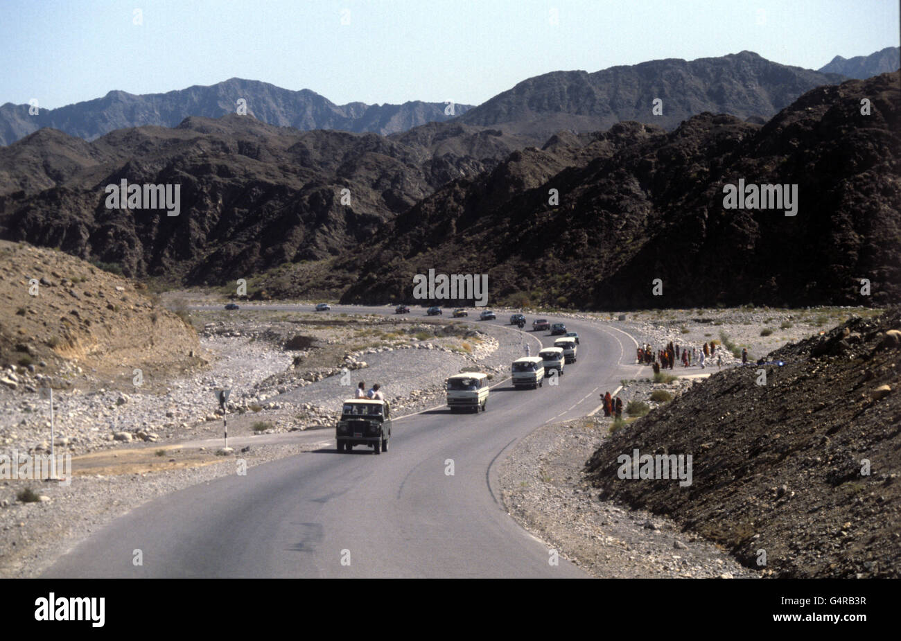 Ein Konvoi, der von einem Pressfahrzeug geführt wird, schlängelt sich während des Besuchs von Königin Elisabeth II. Durch das zerklüftete Land im Oman, auf dem Weg von Muttrah nach Nizwa Stockfoto