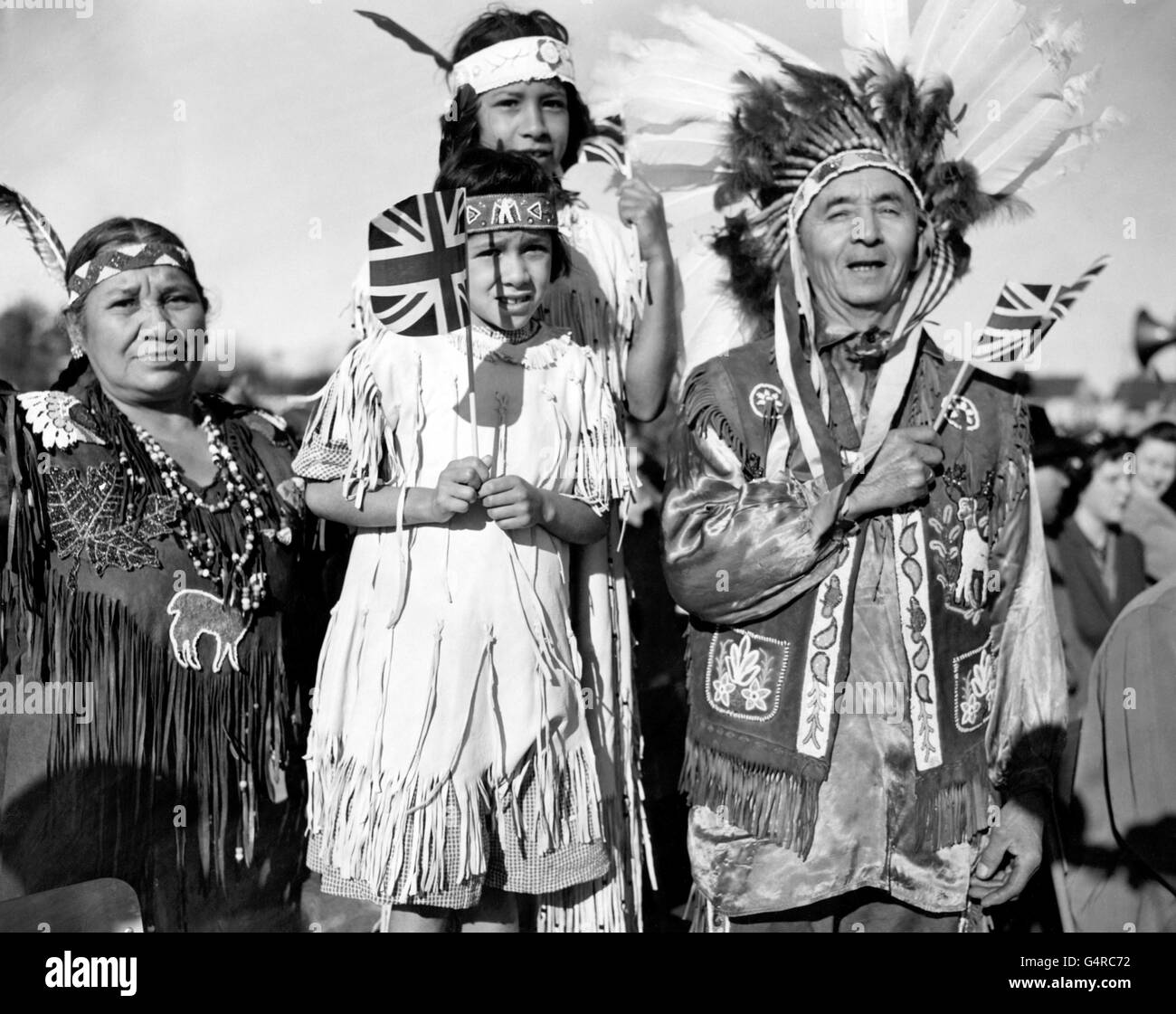 Indianer winken Union Jacks und tragen ihr traditionelles Kleid, darunter ein prächtiger gefiederter Kopfschmuck der Häuptlinge, zu Ehren des Besuchs von Prinzessin Elizabeth und dem Herzog von Edinburgh in Brantford, Ontario, im Rahmen der Royal Tour of Canada. Stockfoto