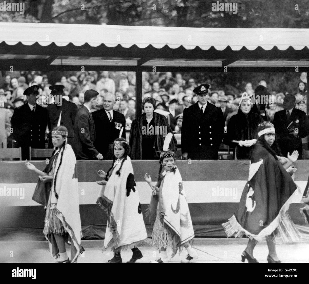 Kleine indische Mädchen in Braves Kostümen und Schuhen im westlichen Stil marschieren herum, klatschen und singen, während sie an einem Indianertanz für Prinzessin Elizabeth und den Herzog von Edinburgh teilnehmen, im Thunderbird Park in Victoria, der Hauptstadt von British Columbia, während der Royal Tour of Canada. Stockfoto
