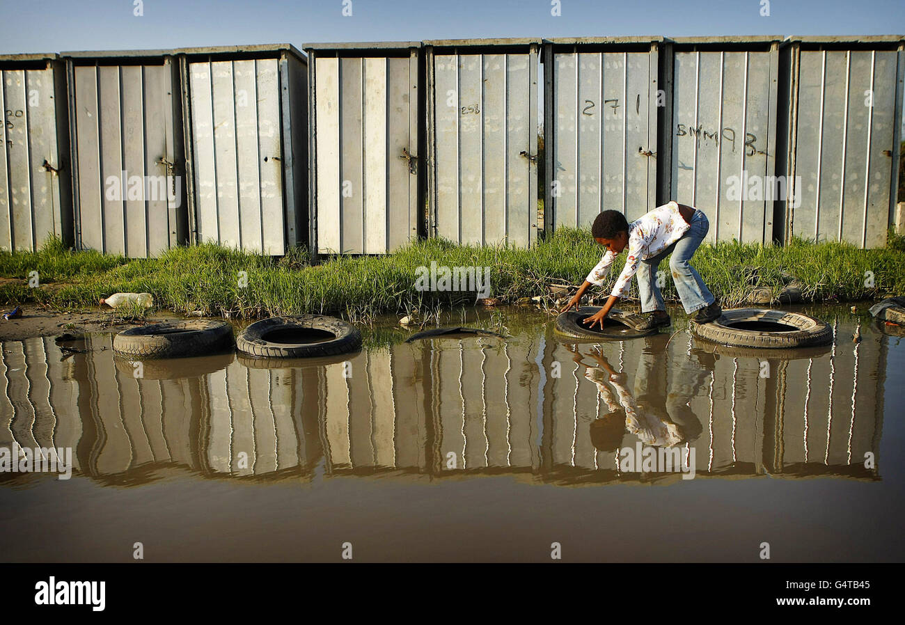 Ein Kind überquert Reifen über Kanalisationswasser, das aus Outdoor-Toiletten im weitläufigen Township Khayelitsha in Kapstadt, Südafrika, austritt Da die Kluft zwischen Arm und Reich in Südafrika zu stark ist, warnte ein ehemaliger UN-Hochkommissar für Menschenrechte. Stockfoto