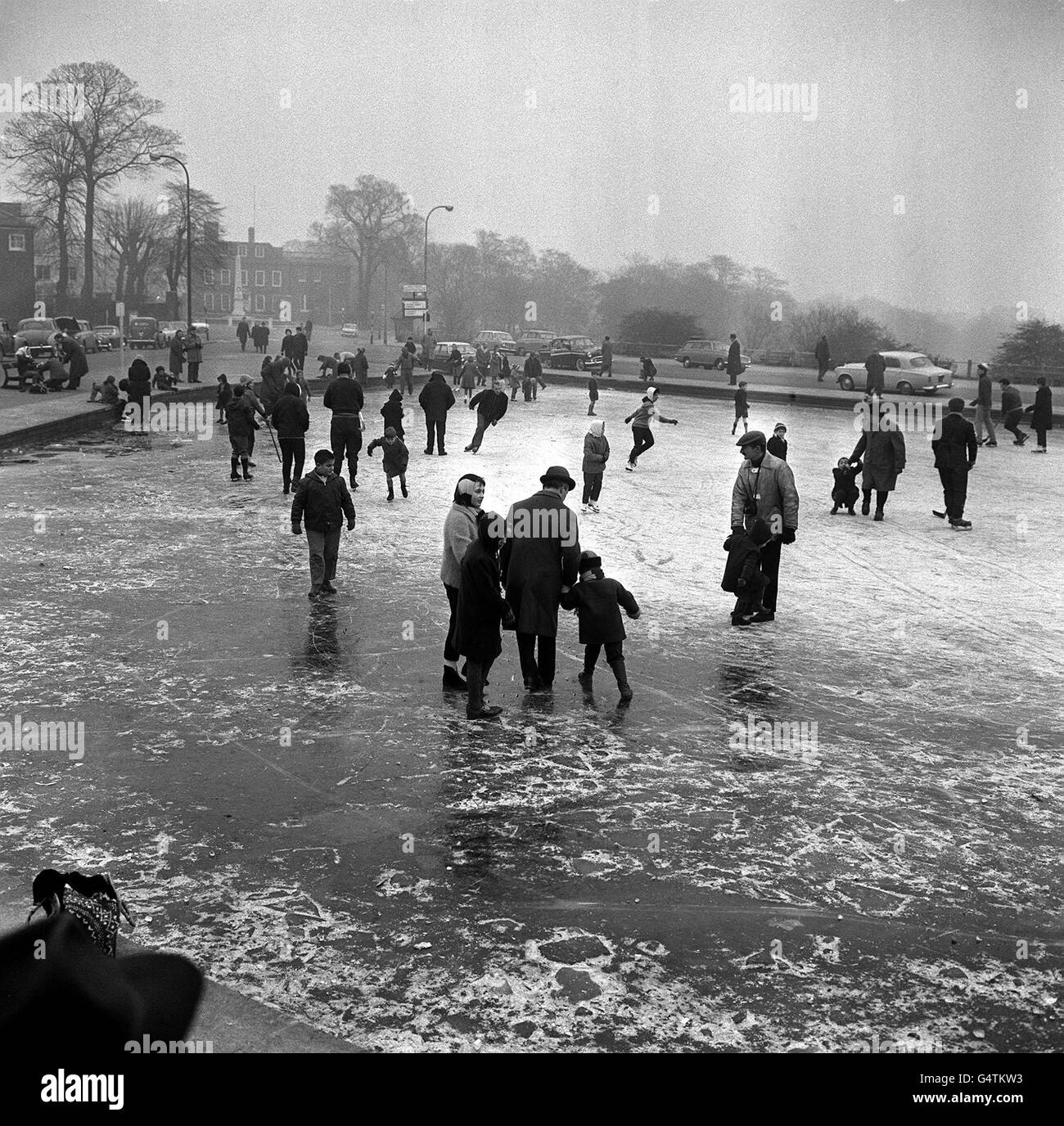 Boxerskater laufen im dichten Eis des Witestone Pond in Hamstead. Auch Menschen, die keine Schlittschuhe mitgebracht haben, genießen die Neuheit, Kinder zu einem Spaziergang auf dem Gebiet zu machen, das normalerweise die Domäne von Modellbooten ist. Stockfoto