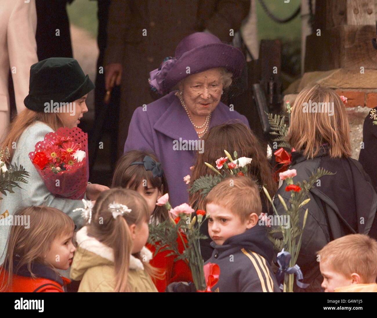 Die Queen Mother (Mitte) wird von ihrer Urgroßmutter Prinzessin Beatrice (links) unterstützt, als sie nach dem Weihnachtsgottesdienst im Sandringham Estate Blumen von Kindern erhält. * die königliche Familie verbringt traditionell die Weihnachtszeit auf ihrem Anwesen in Norfolk, Ostengland. Stockfoto