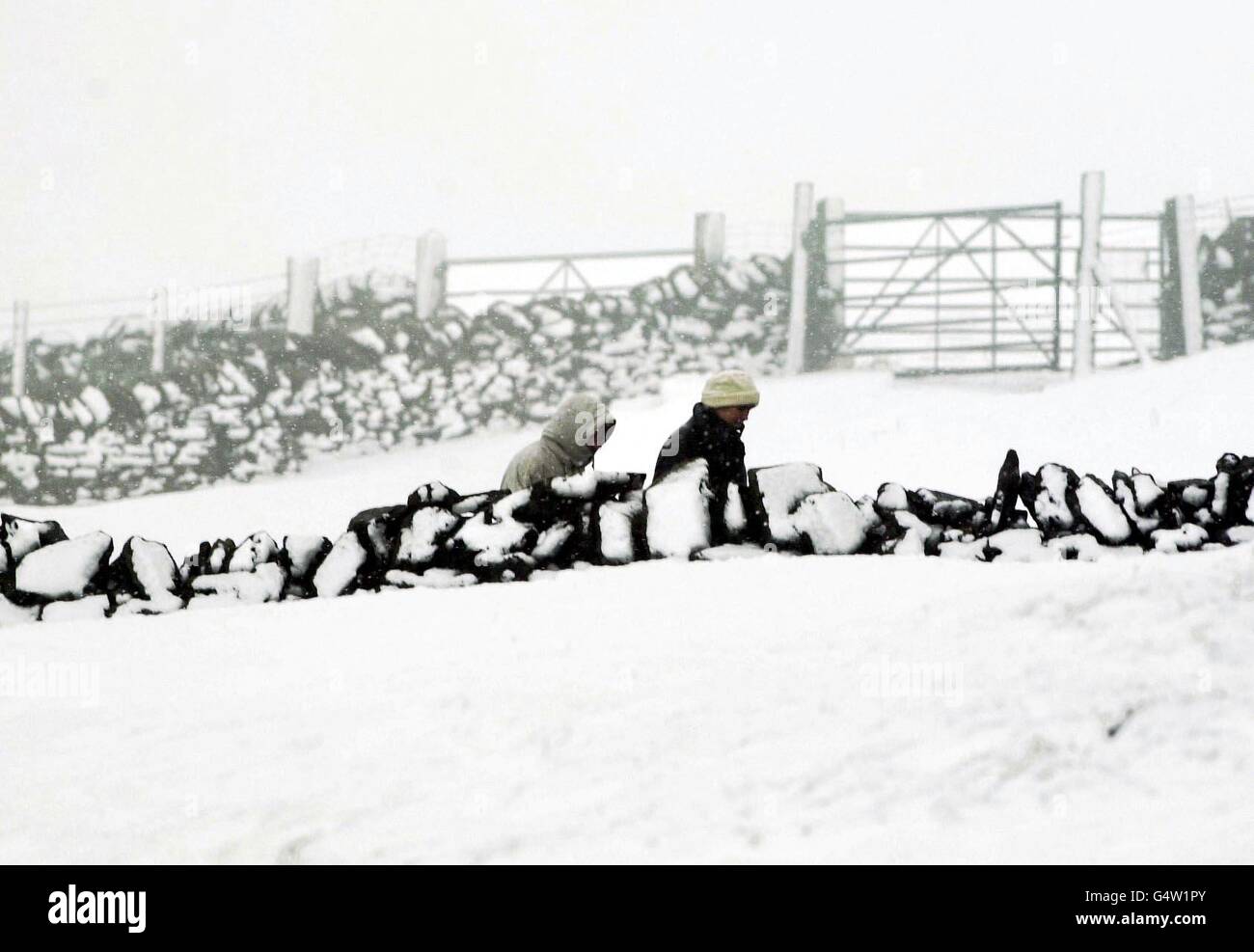 Ein paar Winterwanderer wagen sich auf einen verschneiten Spaziergang auf den Mooren, um Huddersfield herum, wo die Schneeverwehungen so hoch waren wie die Wände. Stockfoto