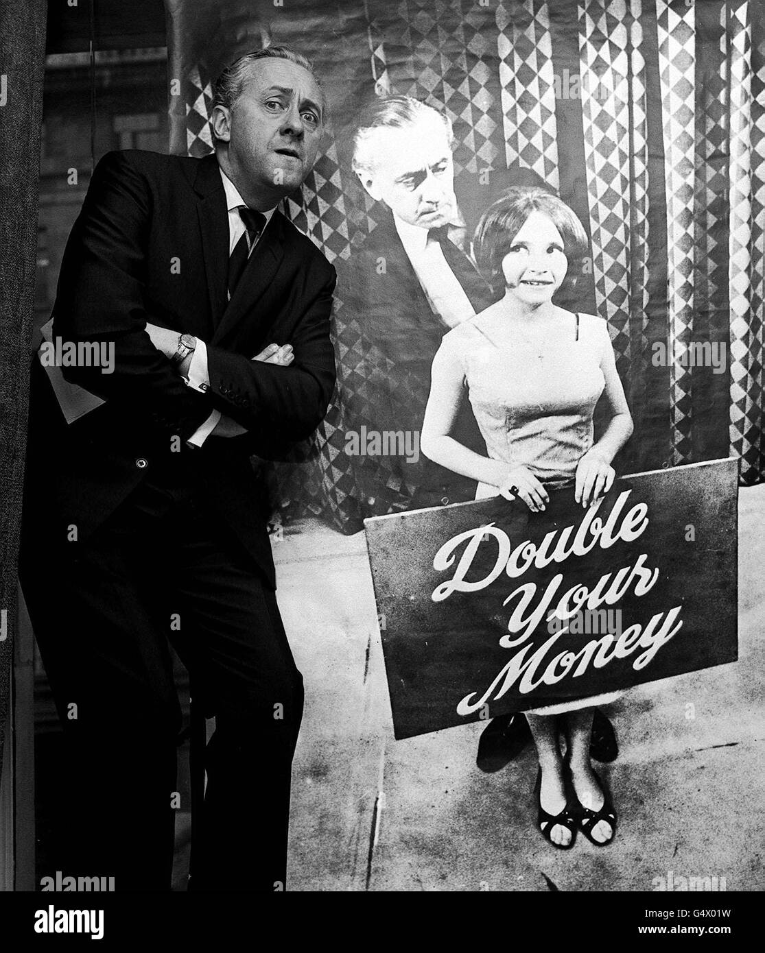 QuizMaster Hughie Green posiert mit einem Poster von sich und seiner Assistentin Monica Rose in London, um das Travel Research Scholarship der Fernsehsendung „Double Your Money“ vorzustellen. Stockfoto