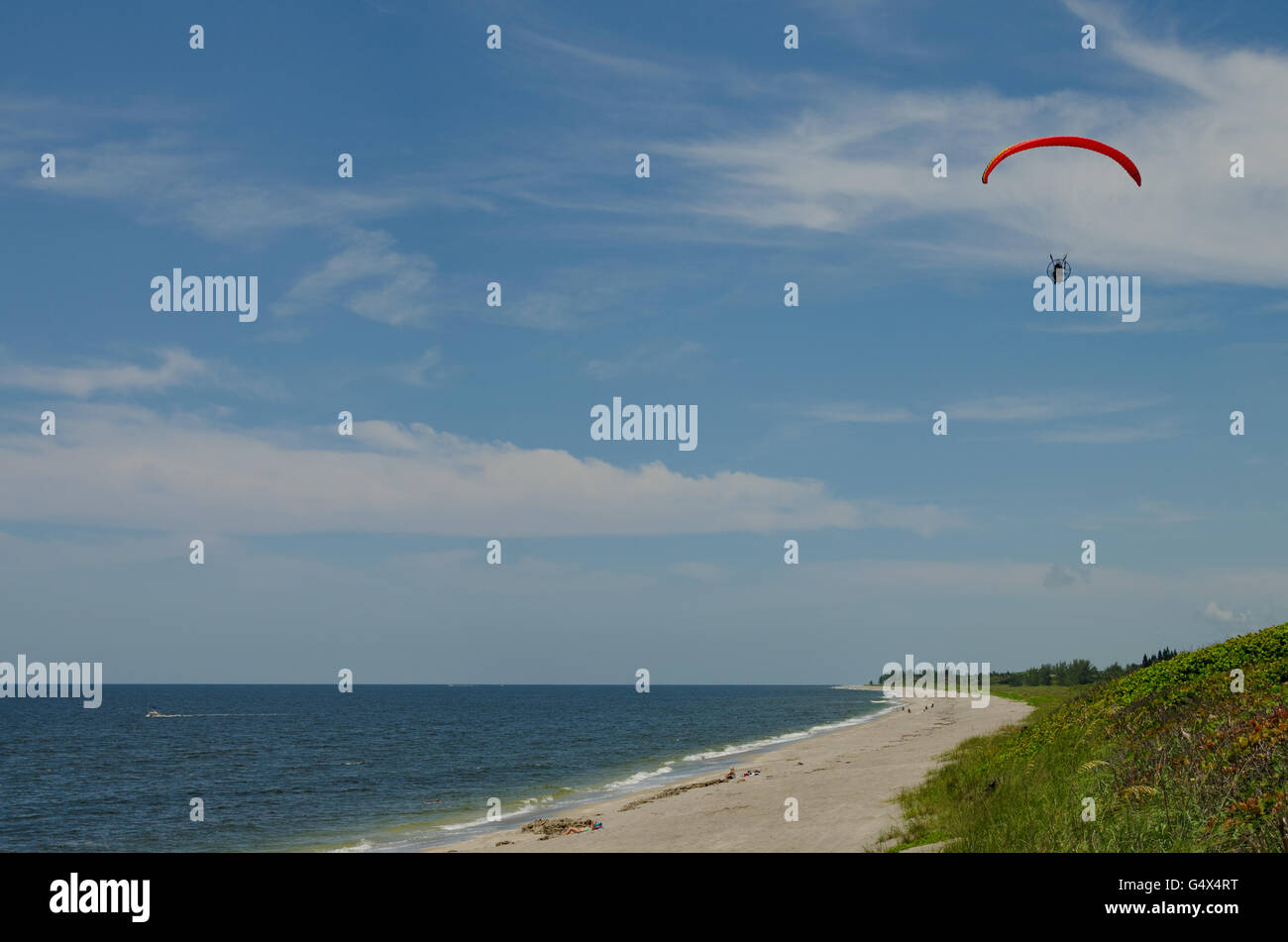 Meer-Strand-Szene mit entfernten Person motor Paragliding vor blauem Himmel Stockfoto