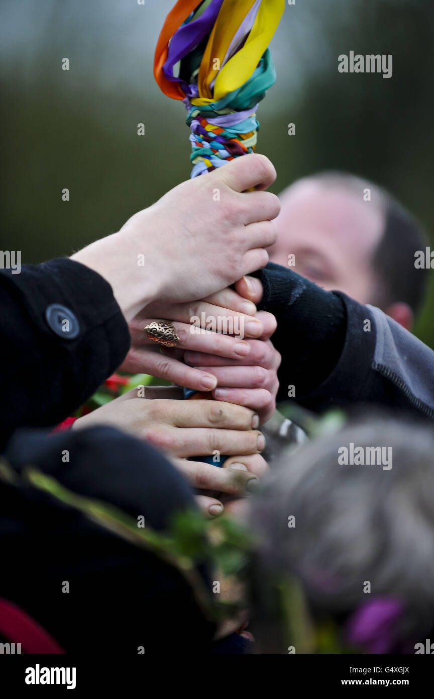 Die Hände werden auf die gewebten Bänder gelegt, nachdem sie am Ende des Maibaum-Tanzes am Avebury Stone Circle, Wiltshire, gebunden wurden, wo die Pagans Beltane feierten, während die Sonne hinter dem wolkigen Himmel aufgeht. Stockfoto