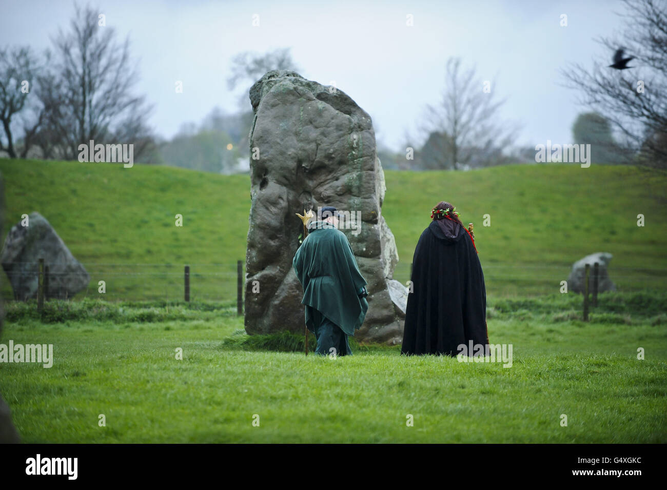 Die Menschen gehen zu dem, was als "Maystein" bekannt ist, um ihm am Avebury Stone Circle, Wiltshire, Respekt zu erweisen, wo die Pagans sich herausstellten, Beltane zu feiern, während die Sonne hinter bewölktem Himmel aufgeht. Stockfoto