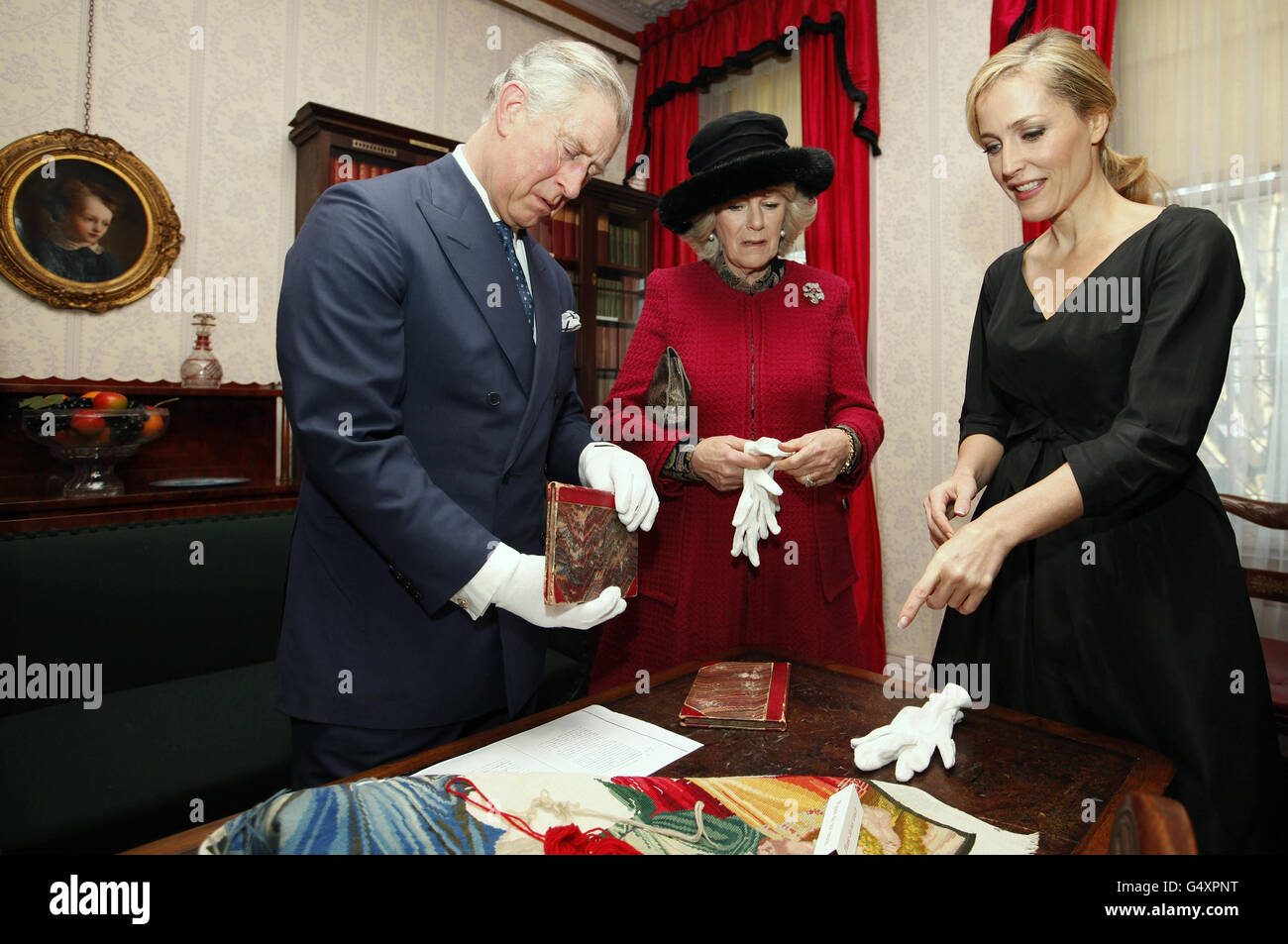 Der Prinz von Wales und die Herzogin von Cornwall, schauen Sie sich zwei Erstausgaben eines Charles Dickens Buches an, während sie mit der Schauspielerin Gillian Anderson in London stehen, um den 200. Jahrestag von Charles Dickens' Geburt zu begehen. Stockfoto