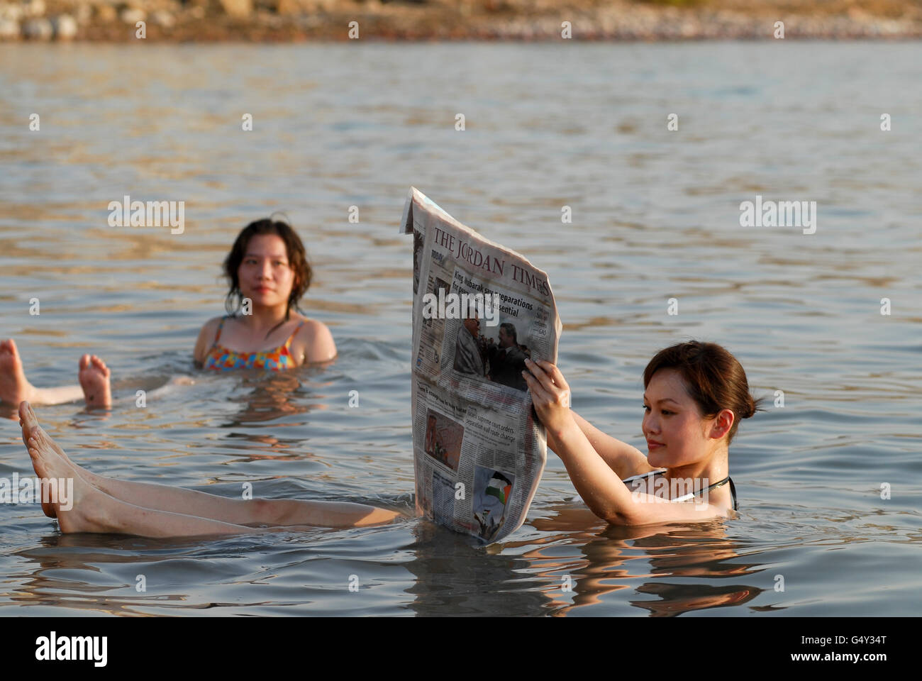 JORDANIEN, Totes Meer, Salzsee, chinesische Touristen Baden und Lesen der Zeitung Jordan Times, Auftrieb durch Salzgehalt, aufgrund des hohen Salzgehalts des Toten Meeres Sie schwimmen auf der Oberfläche ohne Bewegung, Aber der Wasserstand des Toten Meeres ist dauerhaft rückläufig aufgrund des Überverbrauchs von Jordan Flusswasser, die einzige Wasserquelle des Toten Meeres - Auftrieb durch Salzgehalt, hoher Salzgehalt, Medien, Nachrichten, weiblich, Urlaub, Urlaub, Entspannung, ein Bad nehmen, Schwimmen an der Oberfläche, Wellness Stockfoto