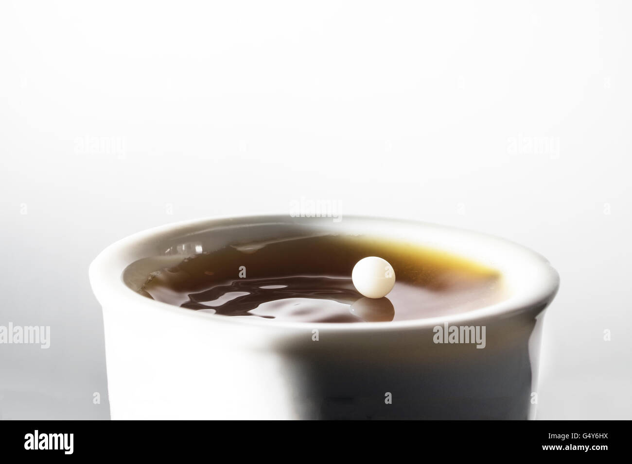 Tropfen Milch balancing und reflektiert an der Spitze, so wie es eine Tasse schwarzen Kaffee trifft Stockfoto