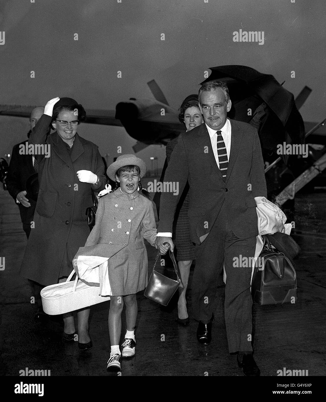 PRINZ RAINIER: Prinz Rainier von Monaco und seine Tochter, Prinzessin Caroline, werden auf dem Weg zu einem Urlaub in Irland von einem Regenschirm vor dem Regen geschützt. Der Prinz wurde so verzögert, dass er seine Tochter direkt in das Flugzeug brachte, das sie nach Irland brachte. Stockfoto