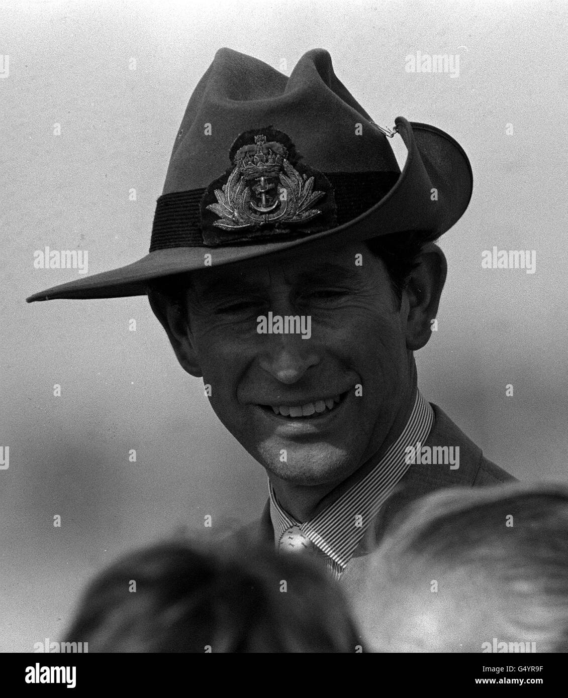 Der Prinz von Wales legt sich einen geliehenen "Zigarrensilz" an, um sich vor der sengenden Sonne zu schützen, während er auf die Versammlung an Bord von HMS Cook lächelt, nachdem er bei ihrer Ankunft im Hafen von Sydney, Australien, den Gruß der Tall Ships übernahmen. Stockfoto
