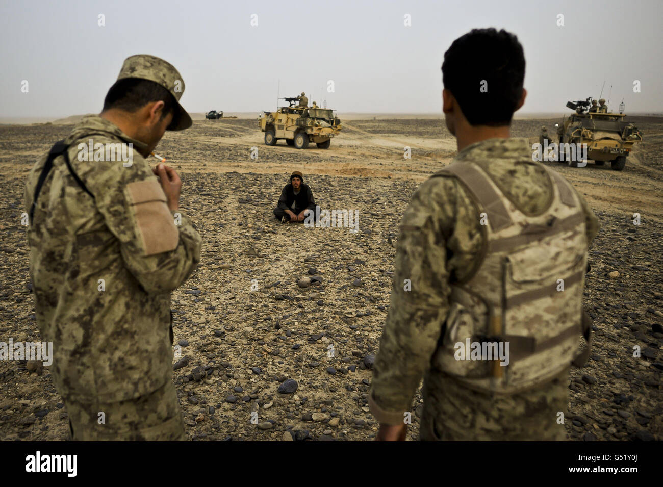 Afghanistan National Order Civil Police (ANCOP) wacht über afghanische Staatsangehörige, während sie sitzen und warten auf die Bestätigung der Identität durch ISAF-Kräfte im Yakhchal-Gebiet der Provinz Helmand gegen Ende des zweiten Tages der Operation "Now Roz" (New Day in in Dari), Die Afghan National Security Force (ANSF) befreit die Taliban aus dem Gereshk-Gebiet der Provinz Helmand, unterstützt und betreut von britischen Truppen, bei der als letzte kombinierte Operation auf Herrick 15 gilt, um die traditionell eine Taliban-Hochburg vom Aufstand zu befreien. Stockfoto