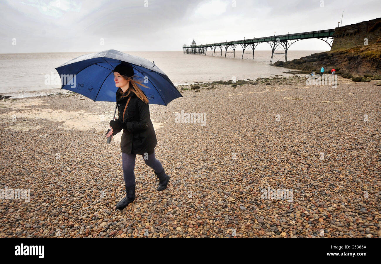 Eine Frau läuft im Regen am Strand neben dem viktorianischen Pier in Clevedon, Somerset. Stockfoto