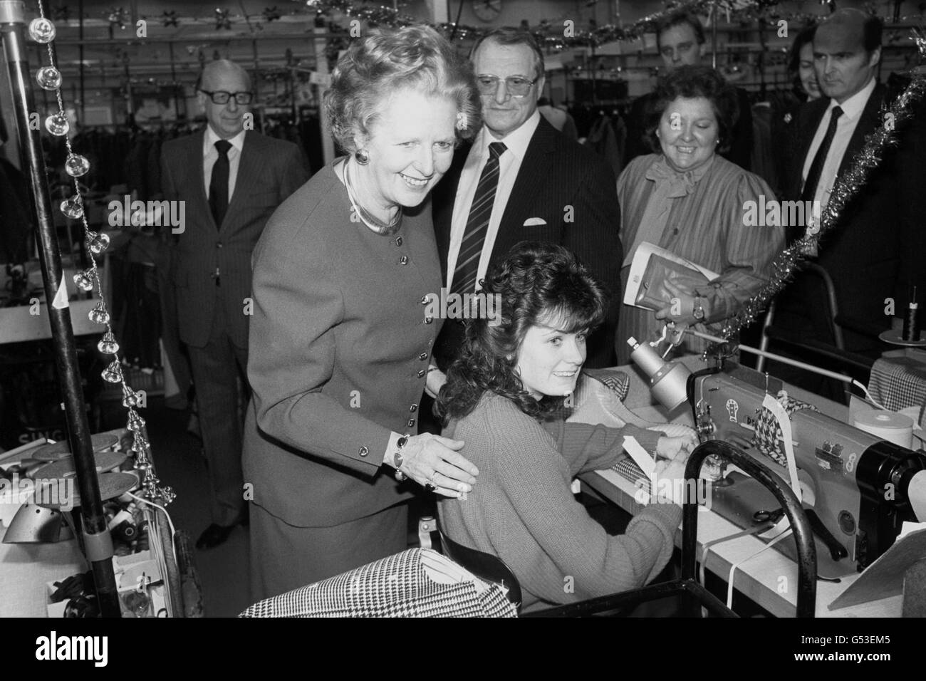 Premierministerin Margaret Thatcher blickt einer Nähmaschinenfahrerin über die Schulter, als sie die Aquascutum-Fabrik in Hemel Hemstead, Herts, besuchte. Frau Thatcher, eine Kundin von Aquascutum, ist die erste britische Premierministerin, die eine der Fabriken des Unternehmens besucht. Stockfoto