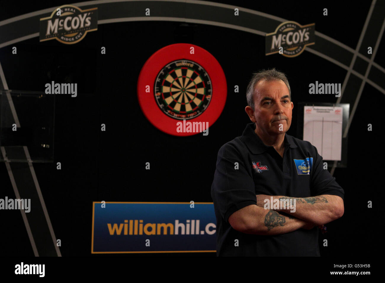 Darts - McCoys Premier League Darts - Capital FM Arena. Phil Taylor trägt sein William Hill Hemd und steht neben der Dartscheibe Stockfoto