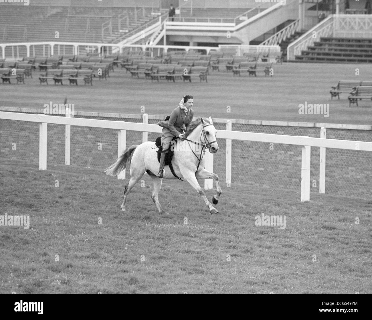 Pferderennen - Queen Elizabeth II - Ascot Racecourse. Königin Elizabeth II galoppiert auf einem grauen Pferd namens „Surprise“ auf der Rennbahn Ascot. Stockfoto