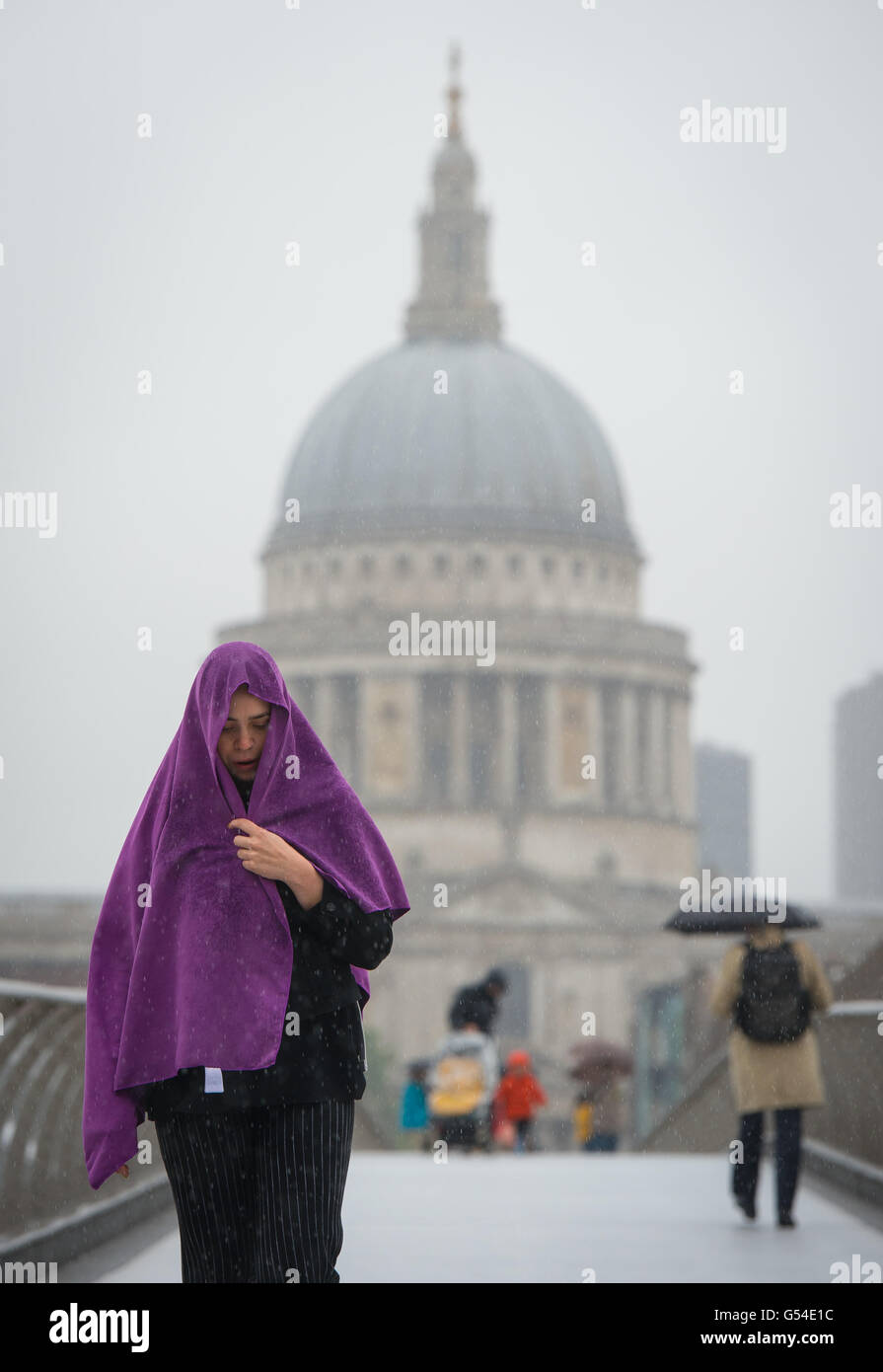 Eine Frau Unterstände unter einen Schal als sie die Millennium Bridge in London und überquert haben als starker Regen und grauem Himmel astronomischen Beginn des Sommers getrübt. Stockfoto