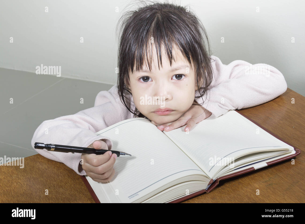 Asiatische Mädchen Kind hart bei der Arbeit im Raum sitzt mit seinem Kopf auf ihre Hand Schreiben von Notizen auf Buch White papers Stockfoto