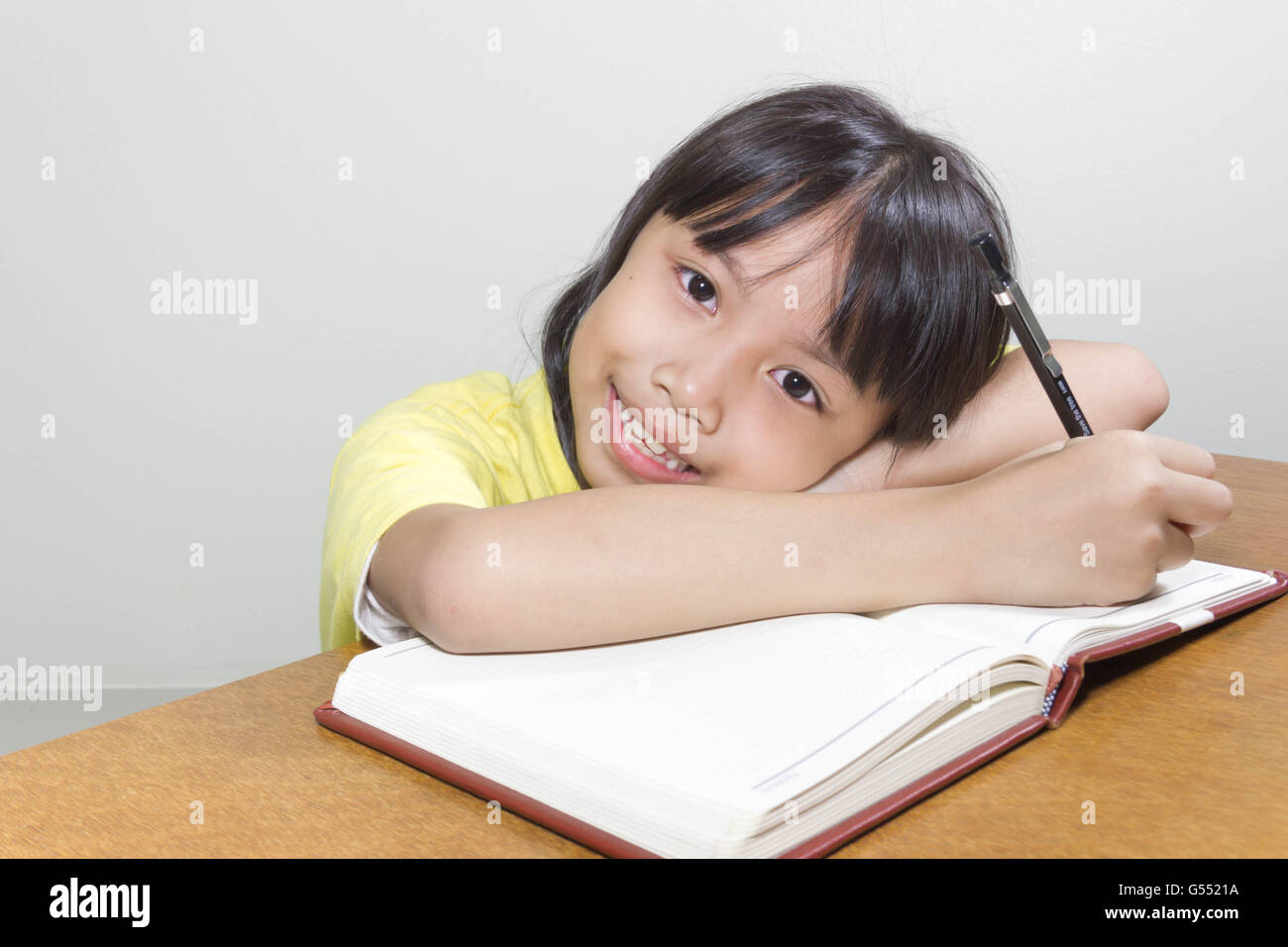 Asiatische Mädchen Kind glücklich arbeiten im Raum sitzen mit ihrem Stift in der Hand Schreiben von Notizen auf Buch White papers Stockfoto
