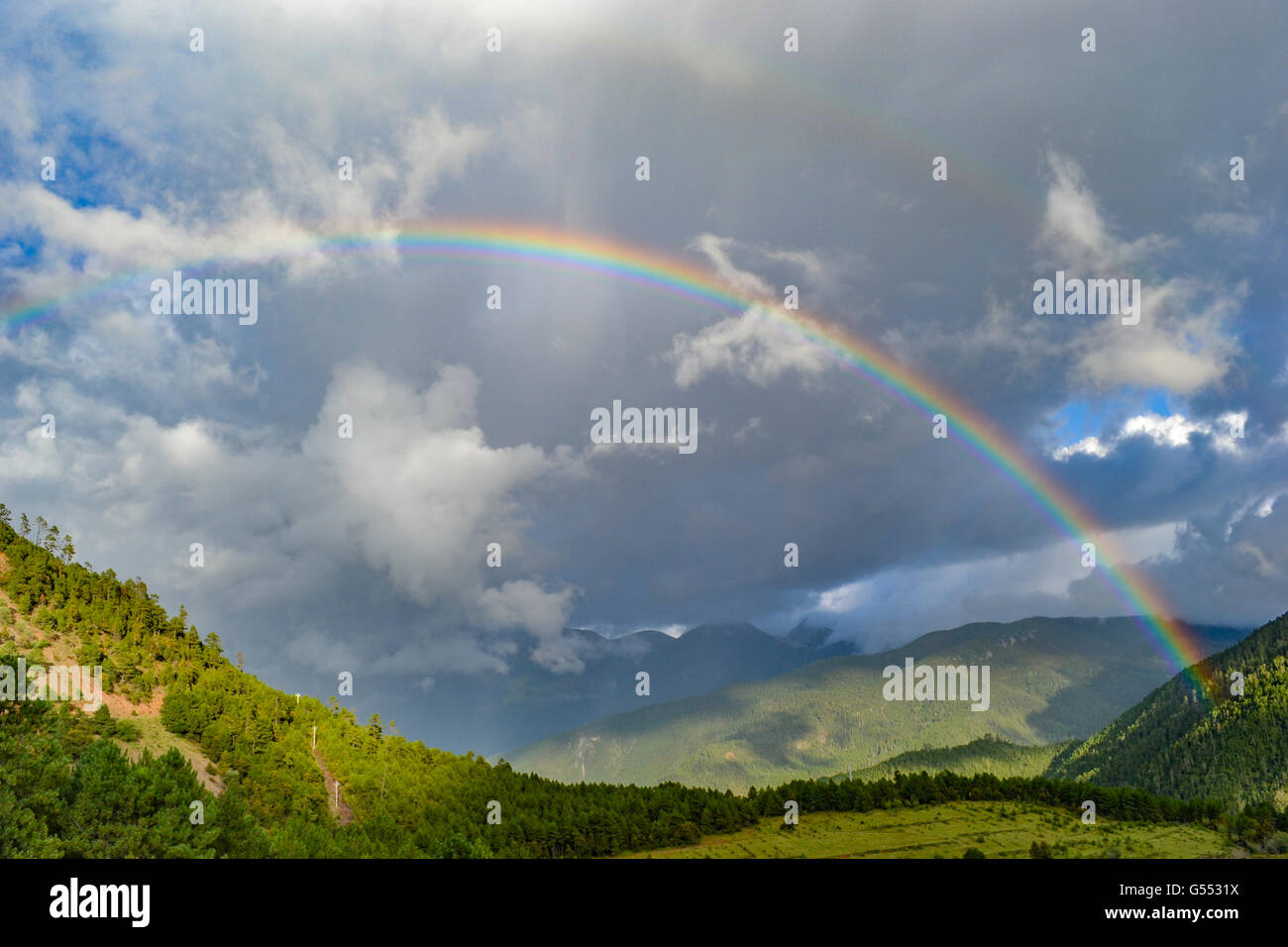 Ein Regenbogen unter den Bergen am bewölkten Tag Stockfoto