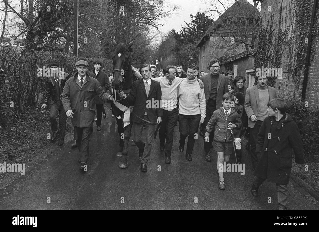 Highland Wedding, Gewinner der gestrigen Grand National Steeplechase, macht durch Fyfield, Hampshire, einen Heldenfortschritt, nachdem er nach seinem Triumph bei Aintree in den Stall von Trainer Toby Balding (mit Brille rechts) mit Jockey Eddie Harty, der Hand auf Pferd hat, zurückgekehrt ist. Stockfoto