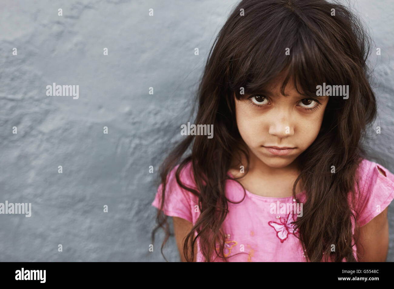 Porträt von preteen Mädchen mit schweren Ausdruck stehen vor grauem Hintergrund hautnah. Weibliches Kind in die Kamera starrt. Stockfoto