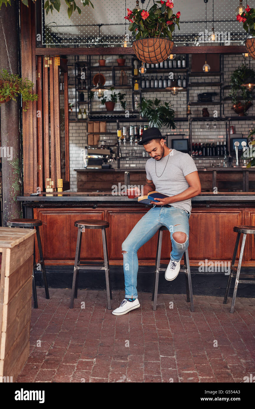 Schuss ein hübscher junger Mann mit Kaffee sitzend mit seinem Buch in einem Restaurant. Kaukasische Männer ein Buch während sitt Stockfoto