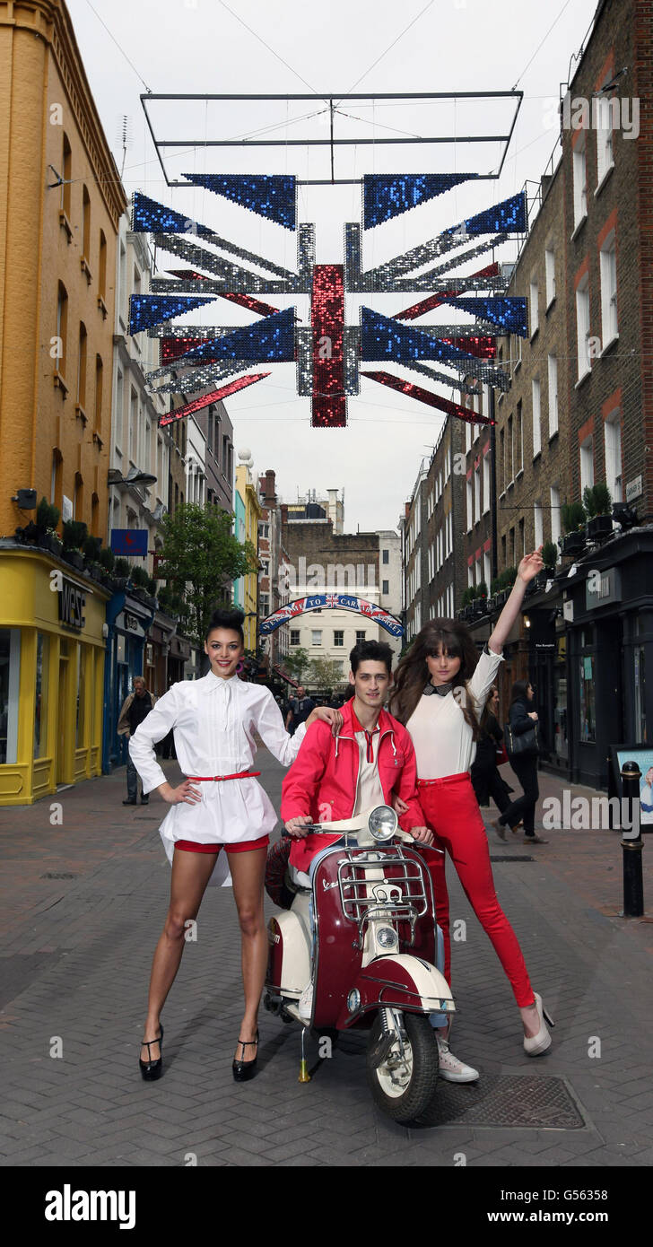 Die Modelle Carlos, Mecia und Jodie stehen unter einer dekonstruierten, dreidimensionalen Union-Flagge, die mit tausenden metallischen roten, weißen und blauen Schimmer-Scheiben bedeckt ist, und hängen über der Carnaby Street im Zentrum Londons als Teil der überdimensionalen öffentlichen Kunstinstallationen für das Diamond Jubilee. Stockfoto