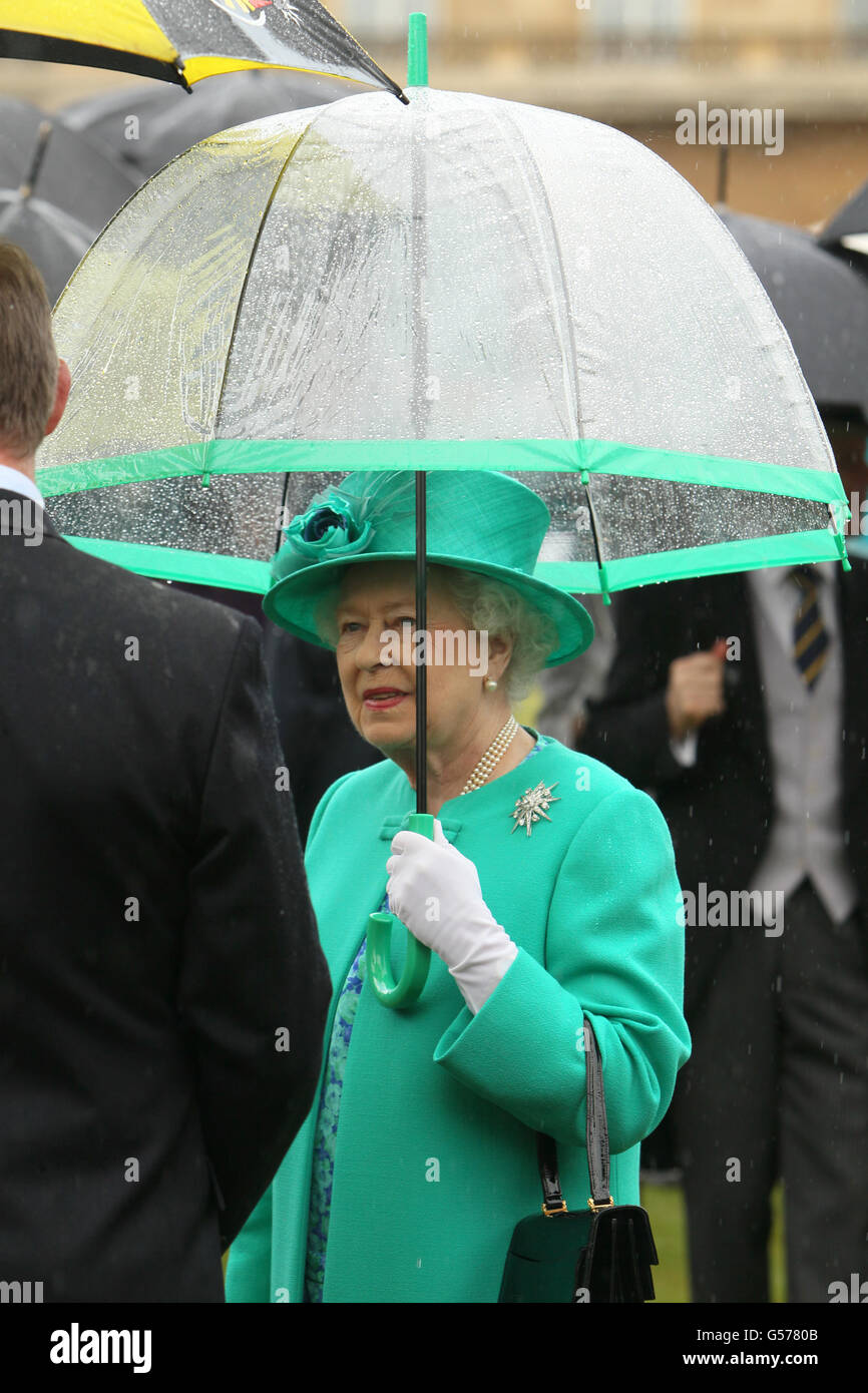 Die britische Königin Elizabeth II. Schützt sich vor dem Regen unter einem  Regenschirm, während sie eine Gartenparty im Buckingham Palace im Zentrum  von London veranstaltet Stockfotografie - Alamy