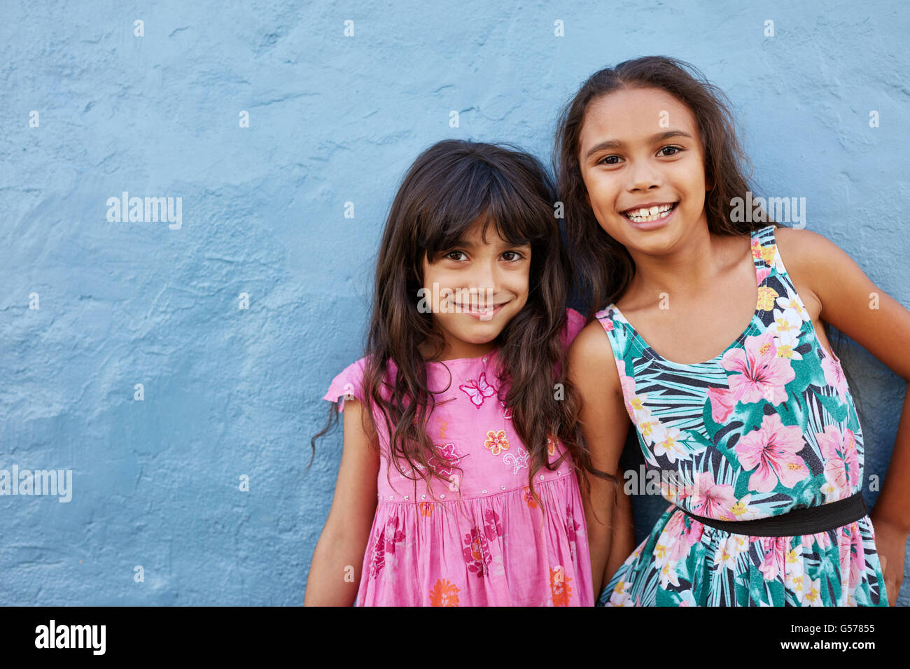 Porträt von zwei kleinen Mädchen vor blauem Hintergrund zusammenstehen. Entzückende kleine Freunde posieren zusammen mit süßen Lächeln. Stockfoto