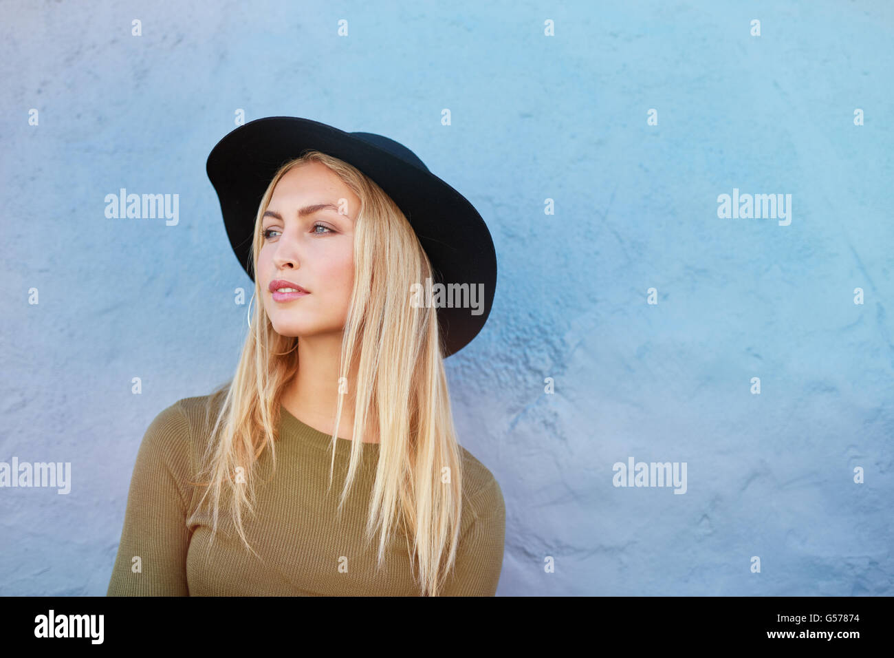 Porträt von attraktiven jungen weiblichen Modell mit Hut wegschauen gegen blaue Wand. Kaukasische junge, blonde Frau mit Textfreiraum. Stockfoto