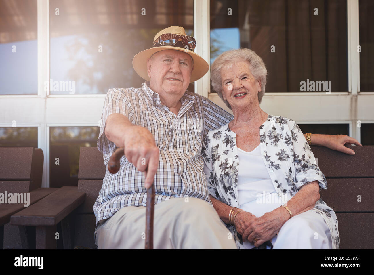 Porträt des Liebens älteres Ehepaar sitzt auf einer Bank vor ihrem Haus. Kaukasische älterer Mann und Frau sitzen entspannt auf einen b Stockfoto