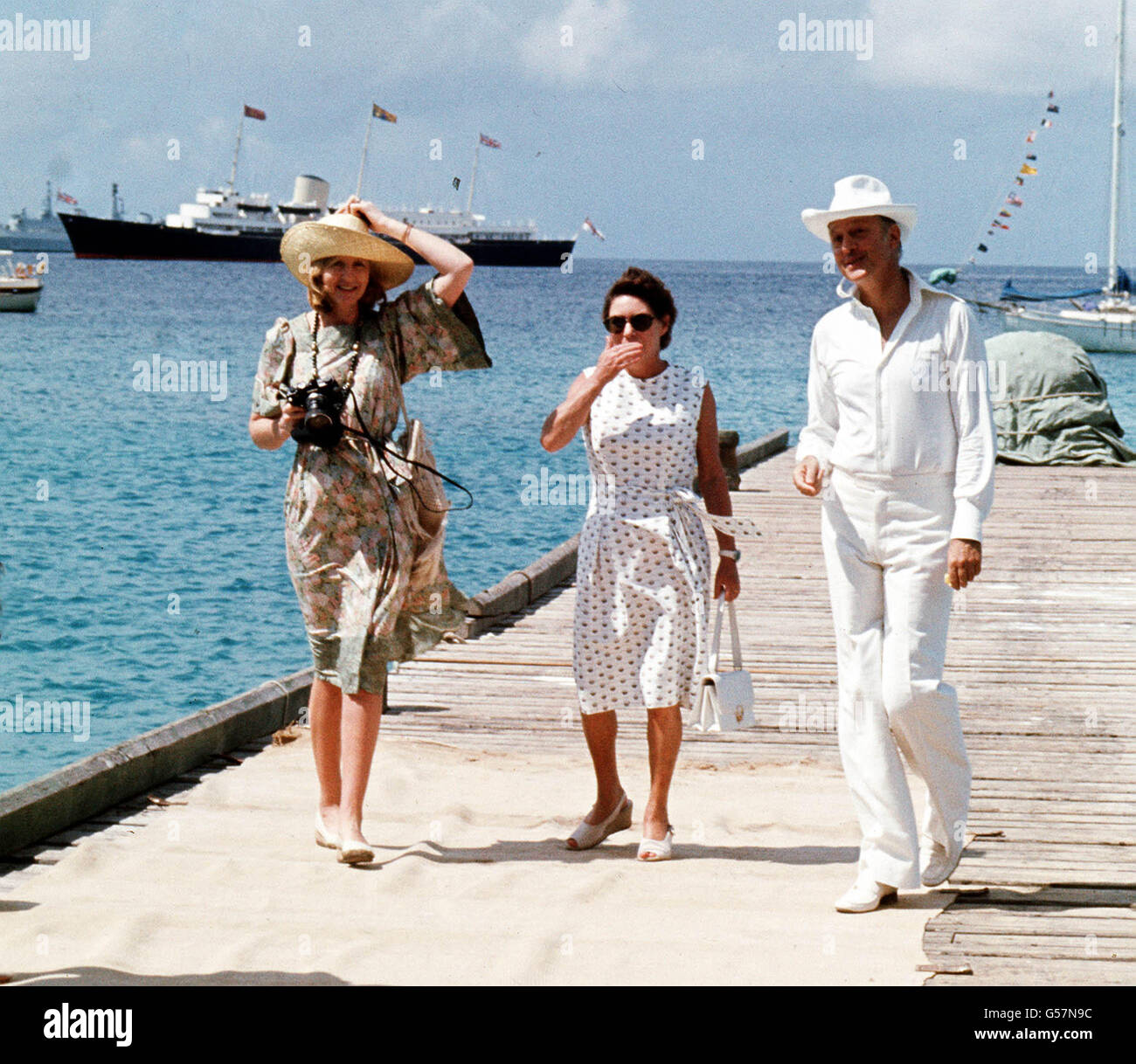 Prinzessin Margaret, Mitte, und ihre Freunde Lady Ann Tennant und Colin Tennant warten auf dem Anlegesteg auf der karibischen Insel Mustique, um Königin Elizabeth II. Zu begrüßen Die Royal Yacht Britannia ist im Hintergrund zu sehen. Stockfoto