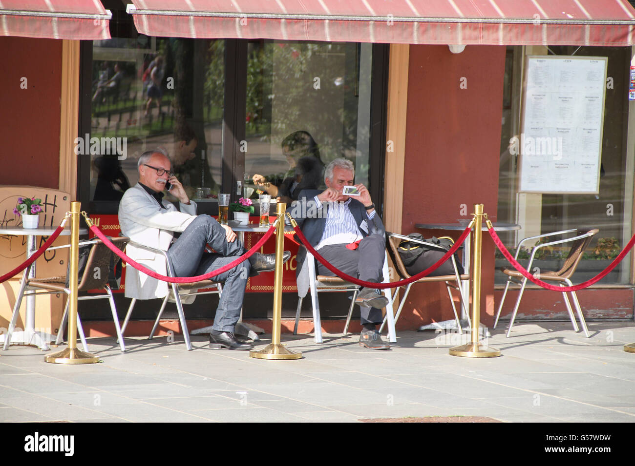 Zwei Männer auf ein Restaurant auf dem Bürgersteig, sowohl mit reden und Betrieb von Mobiltelefonen Stockfoto