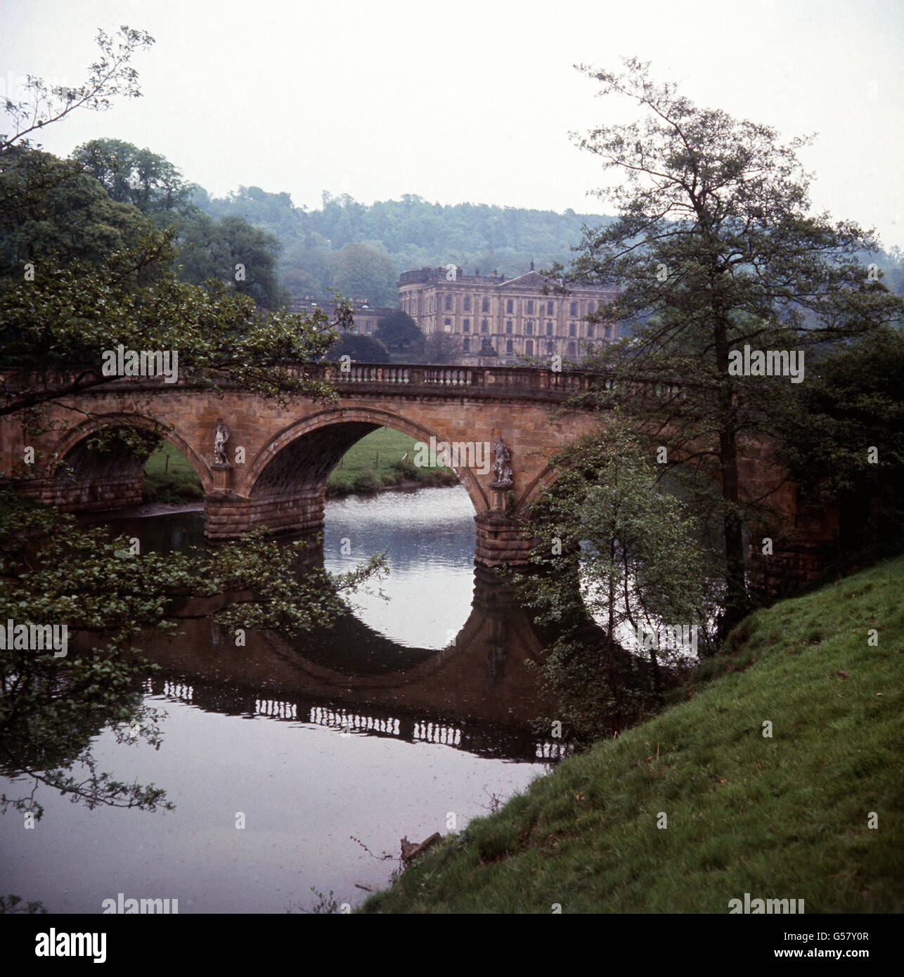 Der Sitz des Herzogs von Devonshire in Chatsworth, Derbyshire. Wasser aus einem großen Stausee auf dem Moor wird über einen Wasserlauf heruntergebracht, um die Brunnen auf dem Anwesen zu bearbeiten. Das Bild zeigt das Chatsworth House und den Fluss Derwent, das Ende der Wasserreise. Stockfoto