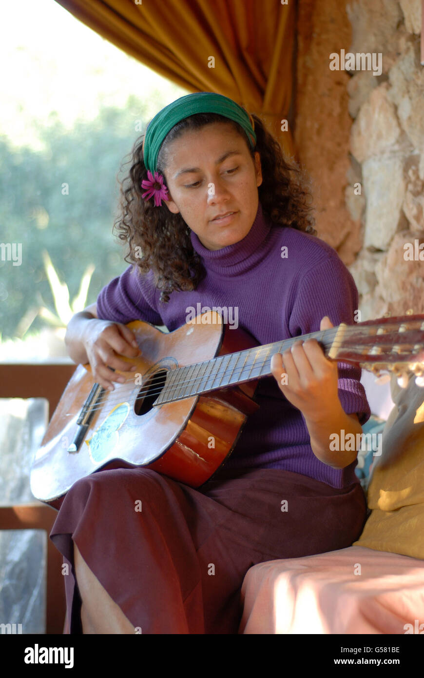 Attraktive junge Brasilianerin spielt Gitarre im Greenheart´s La Casita Verde, Ibiza Stockfoto