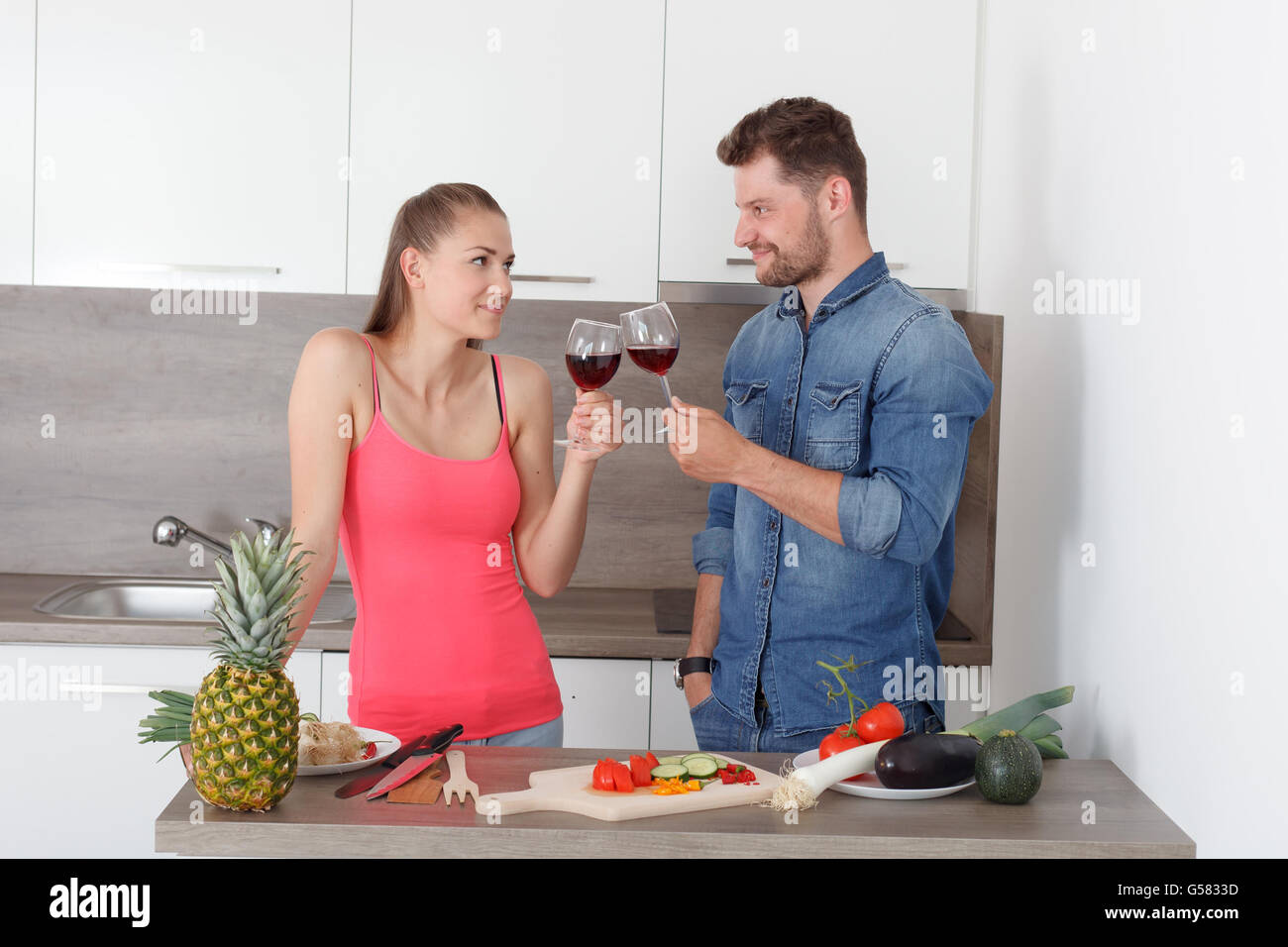 Junges Paar, Mann und Frau feiert die neue, moderne Küche. Schönes Mädchen und sympathische junge mit einem Glas Rotwein. Stockfoto