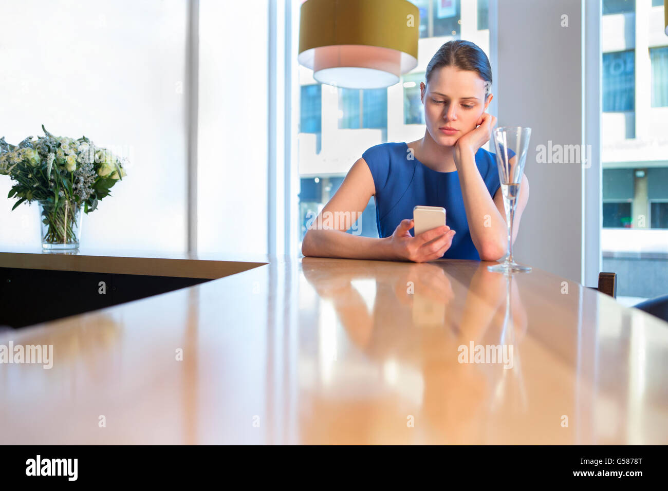 Junge Frau sitzt an der Bar mit einem Glas Champagner, mit ihrem Smartphone. Stockfoto