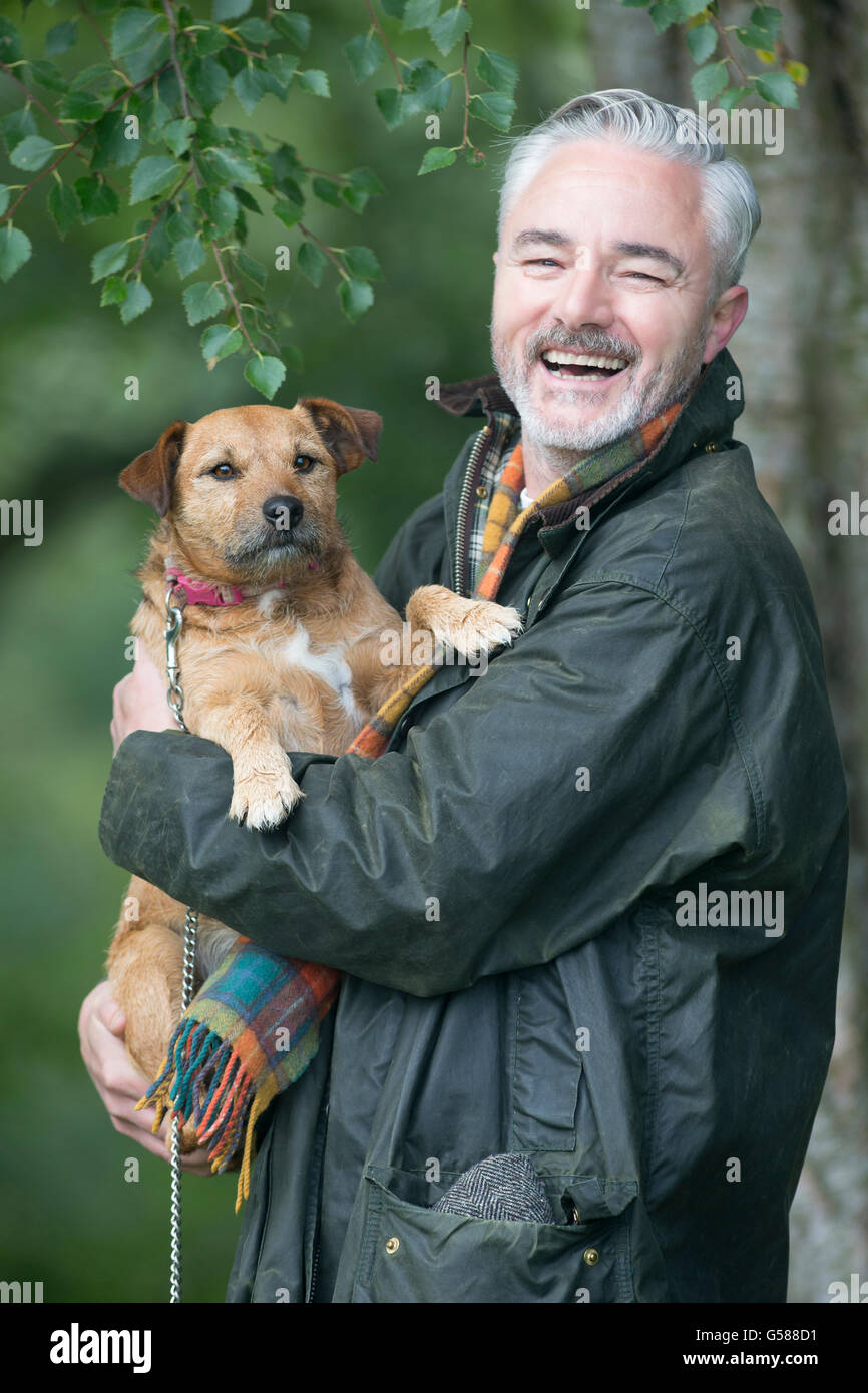 Porträt eines Mannes mit seinem Hund in ein Feld. Er ist für die Kamera Lächeln. Stockfoto