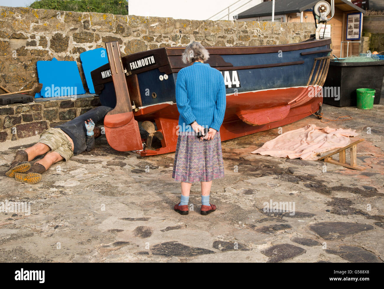 Bild kleines Fischerboot Mann beobachtet von einer älteren Frau vermutlich seine Mutter, Coverack, Cornwall, England, UK Stockfoto