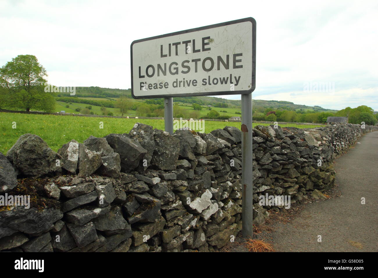 Ein Dorf Schild am Eingang zum kleinen Longstone Dorf, Derbyshire erstreckt sich über eine Trockenmauer, Peak District NP, England UK EU Stockfoto