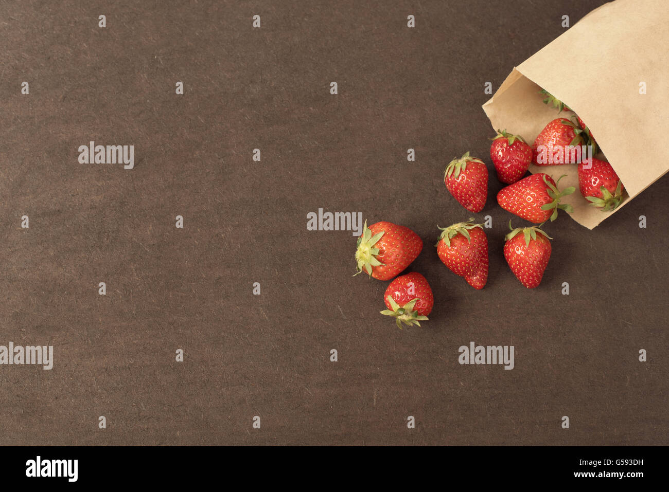 Papier-Tasche mit frischen roten Erdbeeren. Frische Erdbeeren in einer kleinen Tasche auf einer hölzernen Stil Oberfläche. Kleine Gruppe von Erdbeeren Stockfoto