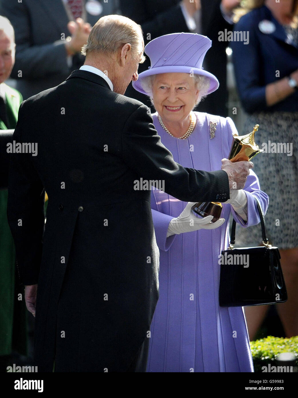 Königin Elizabeth II. Erhält die Trophäe vom Herzog von Edinburgh, nachdem ihr Pferd Estimate am vierten Tag des Royal Ascot Meetings 2012 auf der Ascot Racecourse, Berkshire, die Vase der Königin gewonnen hat. Stockfoto